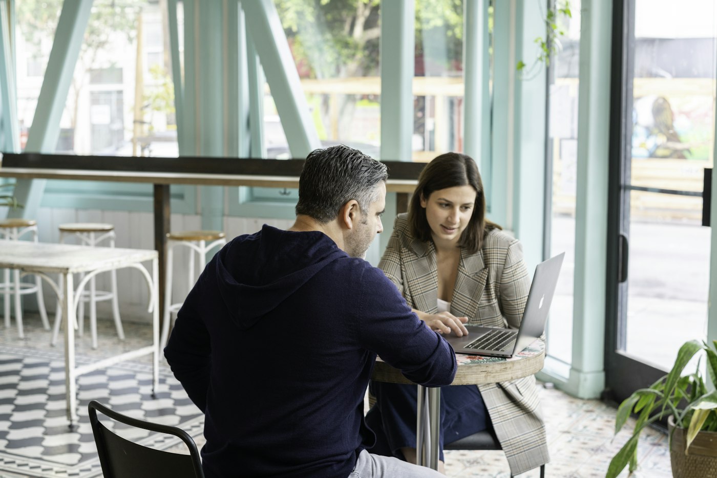 A freelancer and a prospective client reviewing project details together on a laptop at a cafe table.