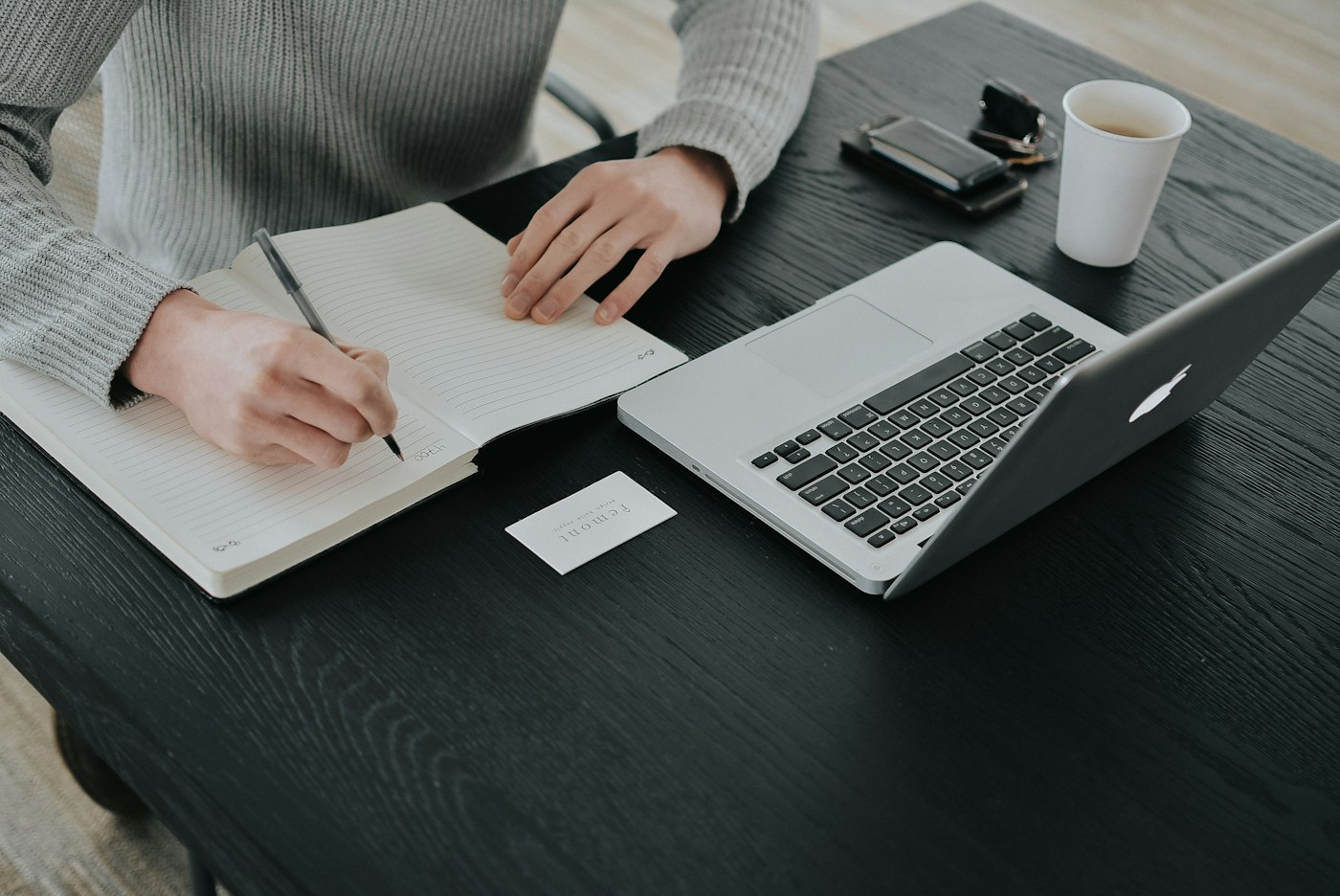 A freelancer writing project notes in a notebook at a desk while preparing the work plan.